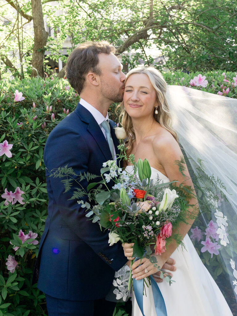 groom kissing bride with sweet soft smile from the bride with soft wildflower bouquet