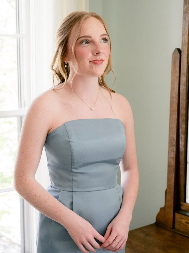 sister of the bride with red hair and blue dress smiling and gazing at her sister getting ready in the bridal suite