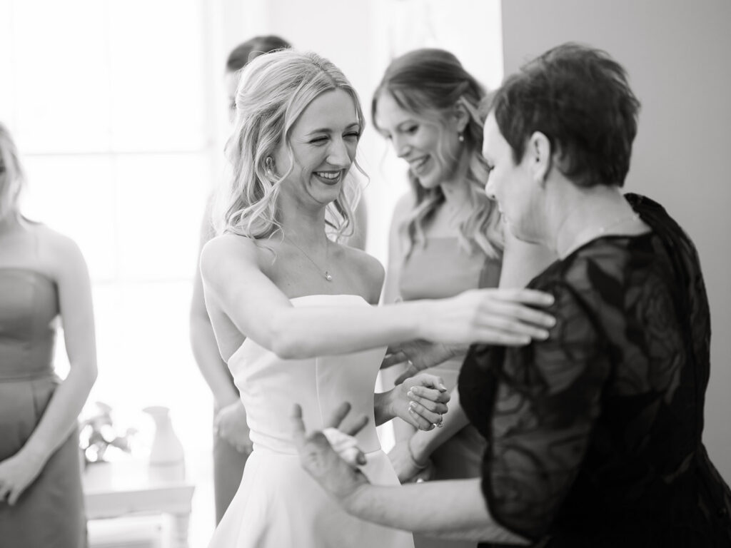 bride and mother of the groom smiling and embracing as they get ready in the bridal suite.