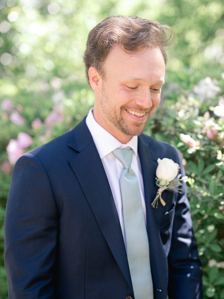groom with blue jacket and white shirt with blue tie looking down with white flower