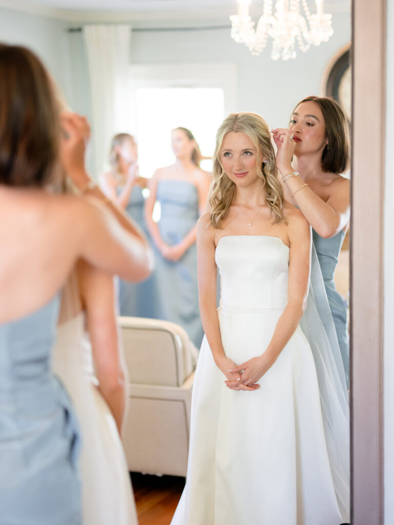 smiling and looking in the mirror fixing the brides hair and putting on the veil