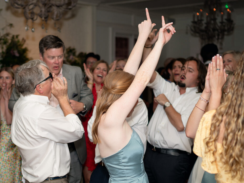bridesmaid putting up fingers in big dance moves as people dance and jump during reception