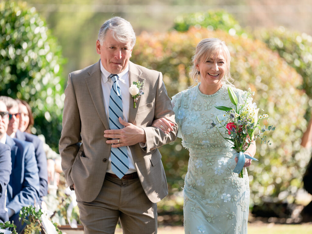 father and mother walking down the aisle with big smiles on their faces