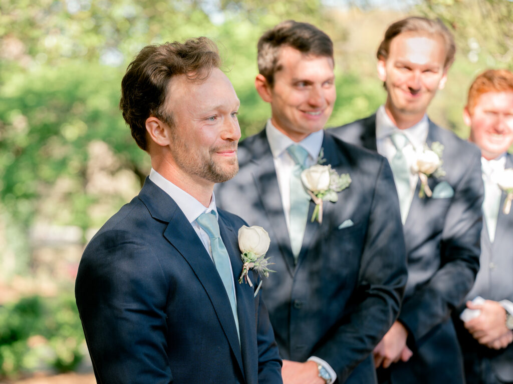 groom looking with big smile down at bride walking down the aisle. dappled light under the tree
