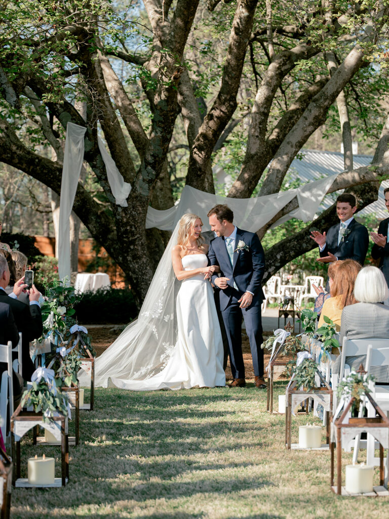 bride and groom under large tree with beautiful white fabric draped all around and through as they have been pronounced husband and wife.